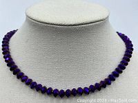 Full view of purple faceted rondelle crystal bead necklace displayed on a mannequin stand showing the shape and length of the necklace.