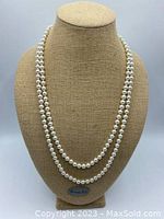 Long white pearl necklace displayed on mannequin in two loops with even drape.