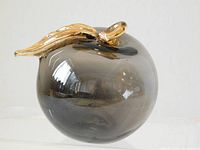 Transparent topaz coloured hand blown glass apple with a gold coloured leaf and stem, showing the right side profile.