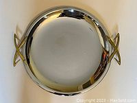 Full view of round chrome tray with visible reflective surface and brass tone thunderbolt shaped handles on each side.