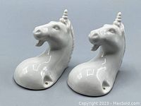 Pair of white ceramic unicorn wall hooks showing front view and glossy surface reflective highlights.