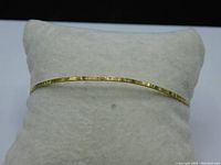 Full view of 14K gold bangle bracelet displayed on a white cushion, showing overall shape and size.