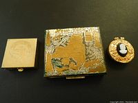 Three vintage metal pill boxes displayed together on a black background, showing front and top designs