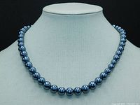 Front view of necklace showing graduated, lustrous black pearls on a neutral display bust.