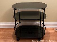 Full front view of the 3-tier black tempered glass cart showing three shelves and metal frame with wheels.