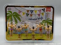 Front view of the Cabana Boys packaged set of 6 muscular male drink markers attached to a backing card with palm tree and festive design