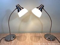 Pair of Hampton Bay LED desk lamps with brushed nickel finish and frosted shades, shown on a wood surface with lamps lit.