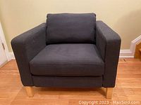 Front angle view of the IKEA Karlstad armchair showing off black fabric, seat and back cushions, and wooden legs.