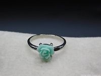 Close-up of silver colored ring band with jade green carved flower top showing front and side view details