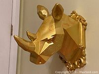 Front angled view of the gold geometric rhino head showing the two horns, ear, and embossed circular patterns.