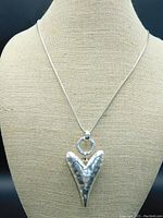 Front view of silver tone hammered puff heart pendant hanging on 36 inch snake chain displayed on beige mannequin.