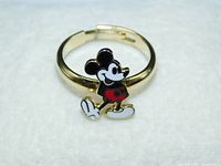 Front view of enamel Mickey Mouse figure on adjustable gold-tone band under bright light on a white background.