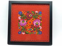 Frontal view of the framed Hungarian Matyó embroidery showing the entire square red wool felt and the colorful floral embroidery with a black frame.