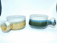 Pair of two vintage stoneware crocks with side handles, one beige and white speckled, one green with blue and white bands, displayed side-by-side.
