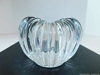 Front view of clear thick glass heart-shaped candle holder with pleated vertical ribs, standing alone on black surface.