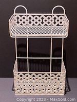 Front view of the vintage white metal wall storage unit showing two-tier design and decorative cut-out pattern.
