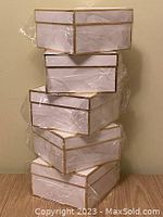 Stack of five white gift boxes with gold trim wrapped in plastic.