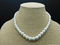 Front view of white pearl necklace on bust, showing graduated pearls from smallest at ends to largest in center.