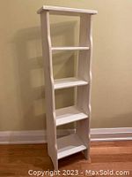 Front side view of slim white painted wood storage unit with four shelves and minor wear.