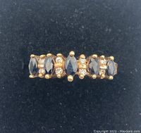 Front view of gold ring showing five marquise dark blue sapphires and the pairs of small diamonds between them against black background.