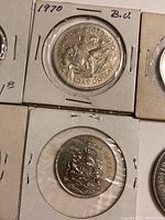 Close-up of 1970 Canada Dollar coin with floral design and one 50 cents coin with Coat of Arms in holder.