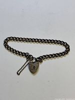Full view of the sterling silver curb link bracelet with heart-shaped padlock charm and safety chain, laid flat on white background.