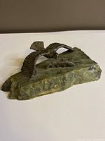 Angled view of pewter eagle and salmon sculpture on green natural stone base, showing eagle swooping toward salmon.