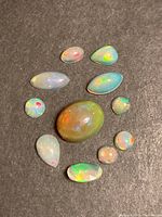 Overview of 11 Ethiopian opal cabochons arranged on black background showing size variations and range of colors.