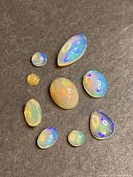 Top-down view of 9 Ethiopian opals arranged on black surface showing color play and various shapes.