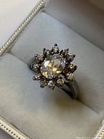 Front view of sterling silver ring with oval central gemstone surrounded by smaller stones in a flower cluster setting in a jewelry case
