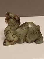 Side view of the jade dragon carving showing details on the neck, head, and body with natural brown inclusions in the green jade.