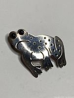 Front view of sterling silver frog pin featuring black onyx eyes and decorative cutouts.