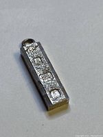 Mini rectangular sterling silver ingot pendant showing hallmark stamps and loop attachment for scale comparison with quarter coin.