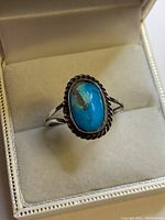 Front view of Navajo sterling silver ring with oval turquoise stone set in twisted rope bezel, displayed in jewelry box.