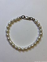 Full view of the pearl bracelet displaying the string of round white pearls and the clasp closed in a circular form.