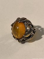 Close-up photo showing detailed silver vine and leaf design and oval amber cabochon stone on ring.