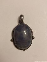 Front view of oval blue cabochon gemstone pendant in stamped sterling silver setting on white background.