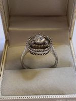 Front side view of the sterling silver ring with central triangular gemstone and two halos of smaller round gems in jewelry case.