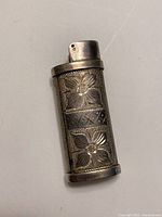 Close-up photo of the front side of the sterling silver lighter holder showing floral and sun engravings.