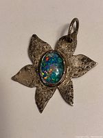 Close-up front view of sterling silver flower pendant with blue-green-orange opal mosaic center under light.
