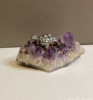 Metal turtle figurine glued onto a natural amethyst crystal cluster base, displaying side profile with visible crystal points and turtle details.