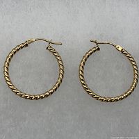 Pair of twisted textured hoop earrings in 14K yellow gold with snap-back closures shown side by side on grey background