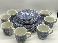 View of the full set showing stacked dinner and luncheon plates with cups arranged around them. Blue and white hunting designs are clearly visible.