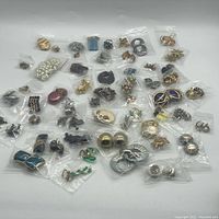 Full lot of 55 vintage earrings individually bagged, showing wide assortment of styles and shapes, mostly clip-on.