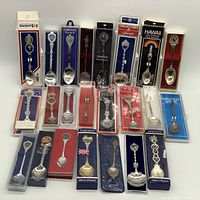 Top view of 20 assorted souvenir silver plated spoons in original packaging showing various locations and themes.
