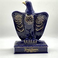 Front view of blue ceramic eagle decanter with gold detailing and base lettering.