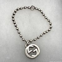 Full view of the Gucci sterling silver bracelet with round bead chain and interlocking G pendant, laid flat and closed in circle shape.