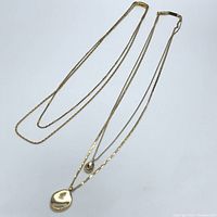 Full view of two gold-tone layered necklaces laid flat showing chains and pendants.