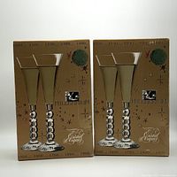Two boxed sets of Millennium Cristal d'Arques champagne glasses, showing front of packaging with glass silhouette, logos, and decorative starry pattern.