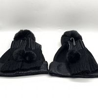 Front view of black ribbed knit beanie and matching fingerless gloves, showing large and small faux fur pom poms respectively